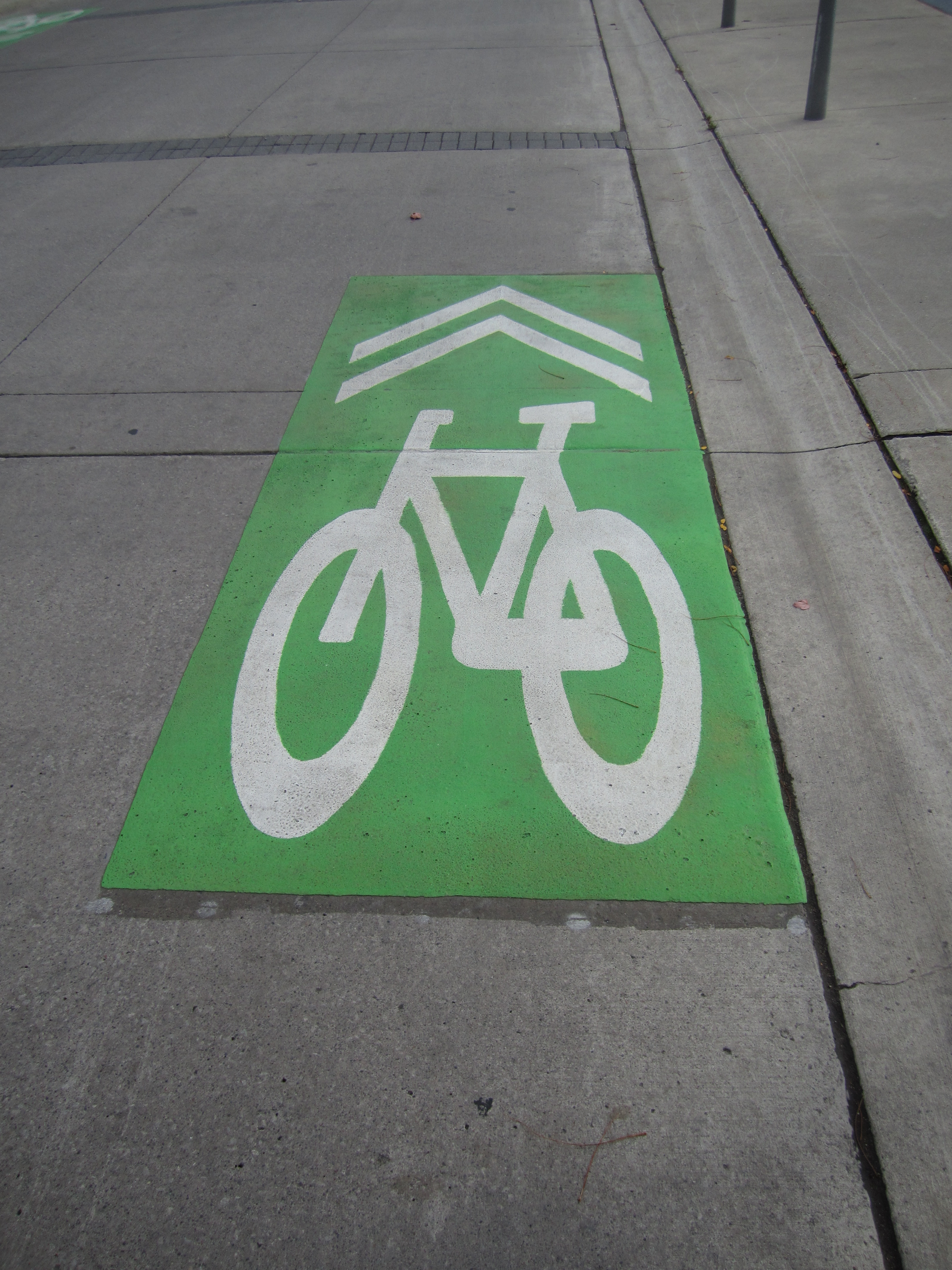 a picture of a white painted bike symbol with double arrows ontop of a green square background 